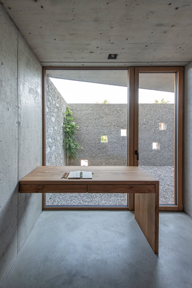 Timber desk positioned in front of glazed doors overlooking a planted courtyard with aggregate walls