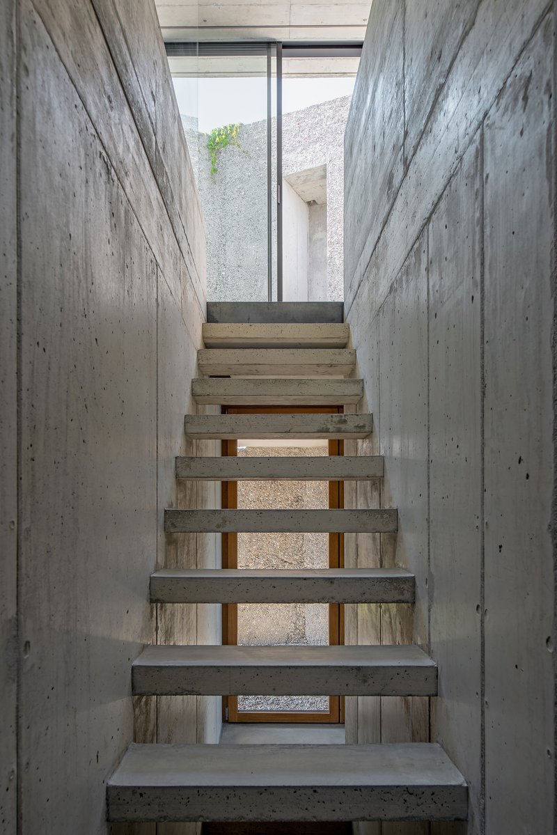 Concrete staircase with open risers framed by board-formed walls and a clerestory window above