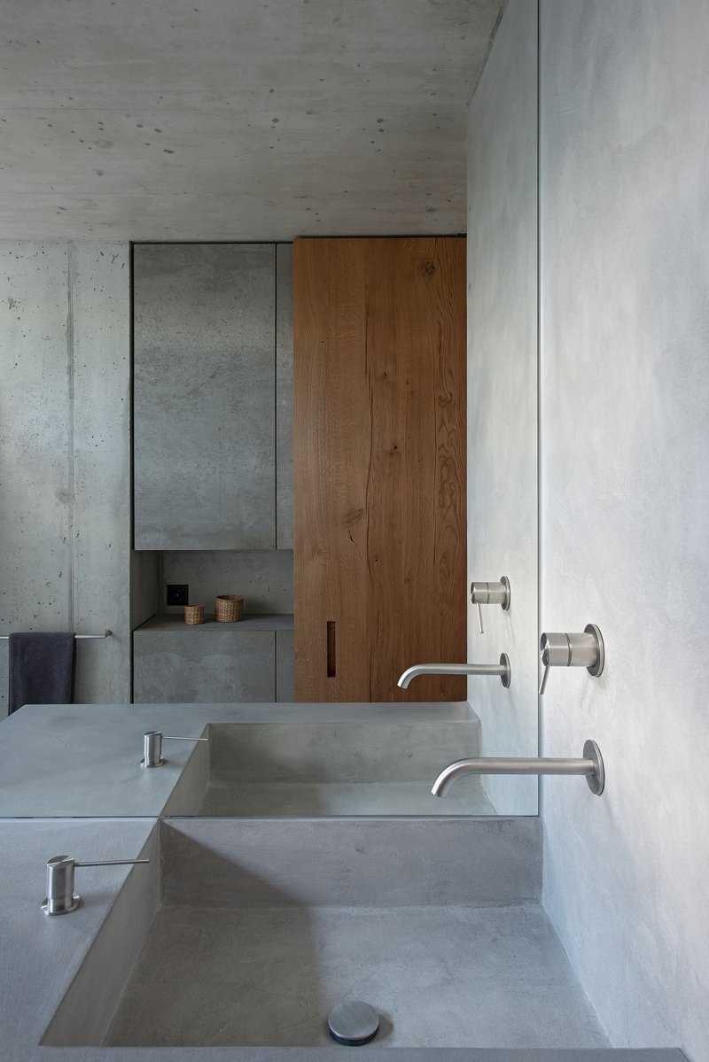 Concrete bathroom vanity with integrated sinks and wall-mounted faucets beneath wood paneling