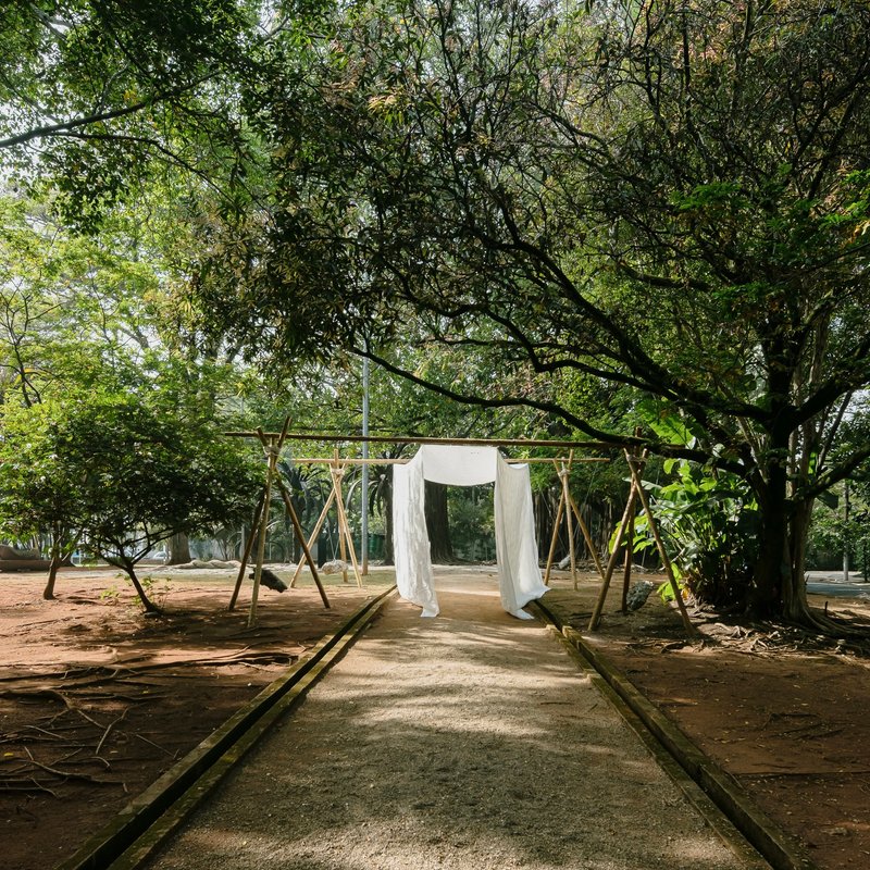 Timber frame pavilion with white fabric panels along a paved pathway beneath a canopy of trees