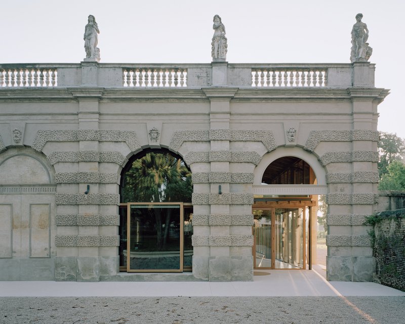 Rusticated stone gateway with arched openings flanked by new bronze-framed glass doors at dusk