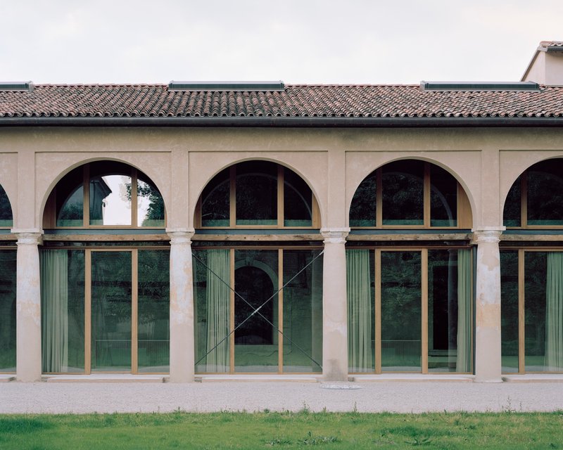 Arcade facade with arched openings and glazed bronze-framed doors beneath a tiled roof