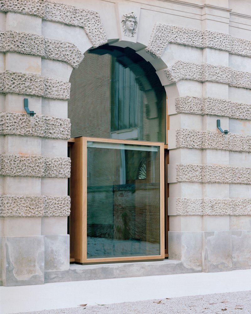 Bronze-framed glass window inserted into a rusticated stone facade with arched opening above