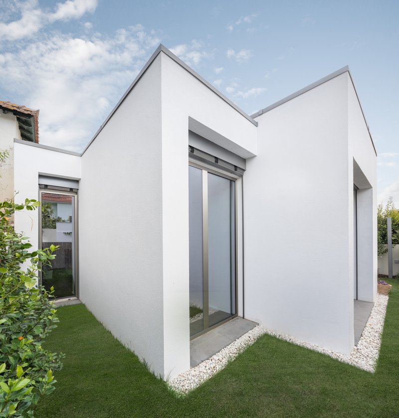 White rendered gabled volumes with sliding glass doors opening onto a lawn under scattered clouds