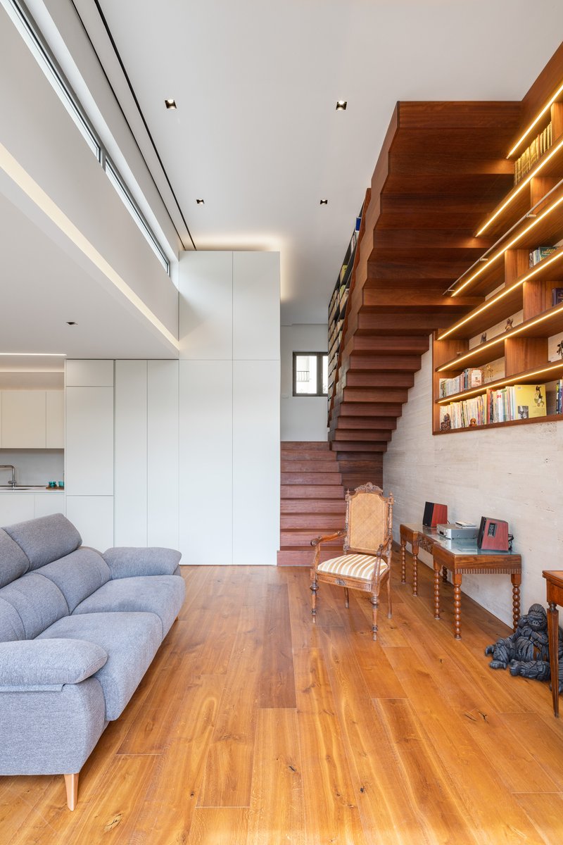Open living space with floating stair linking timber shelving wall and white kitchen under clerestory windows