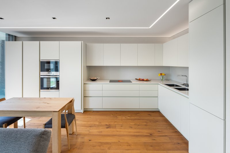 White kitchen with handleless cabinetry and continuous cove lighting above oak timber floors