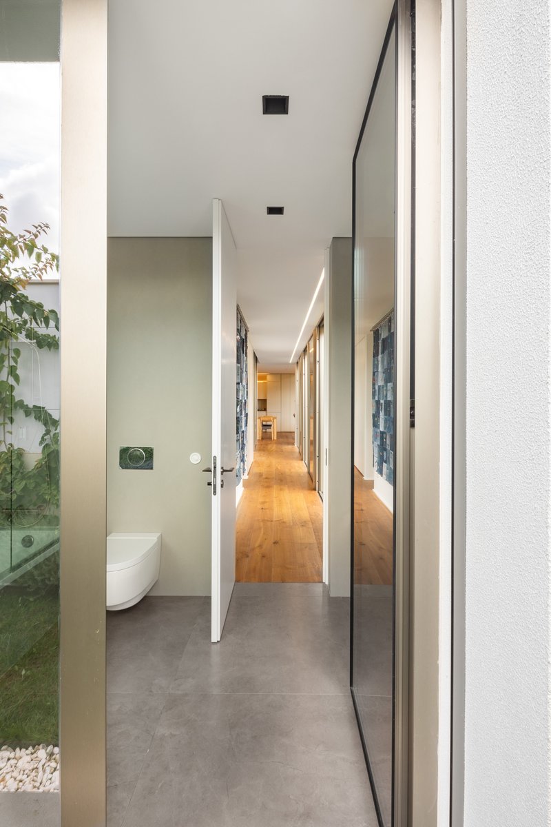 Interior hallway with polished concrete floor looking past a bathroom door toward timber flooring beyond