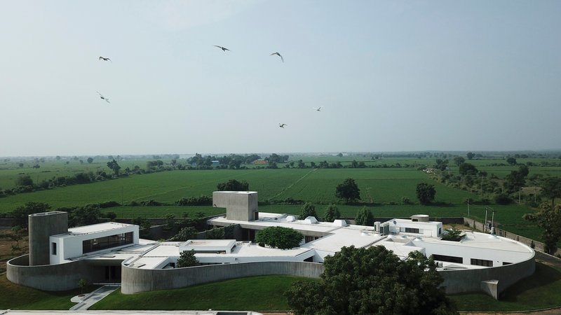 Aerial view of the curved white concrete volumes arranged around a central courtyard with birds overhead