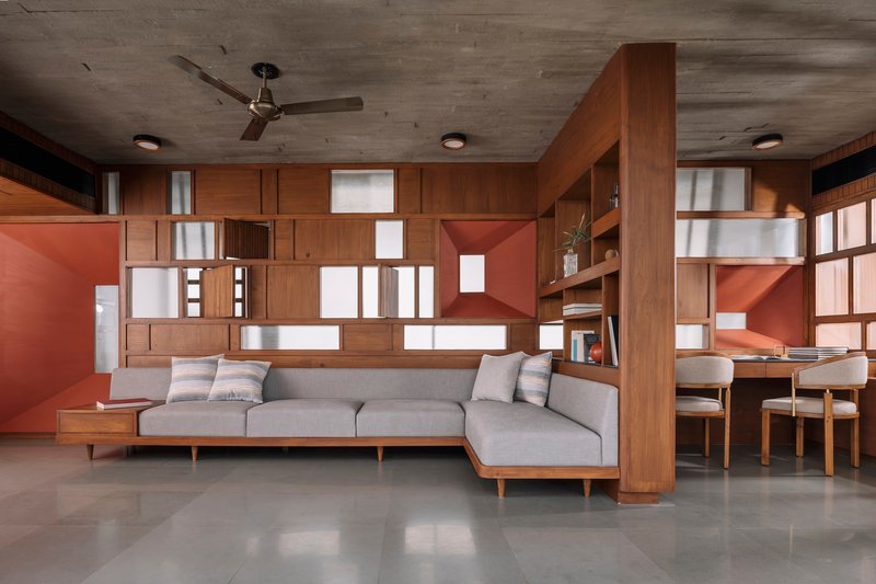 Living room with grey sectional sofa below a gridded timber and terracotta wall system with recessed lighting
