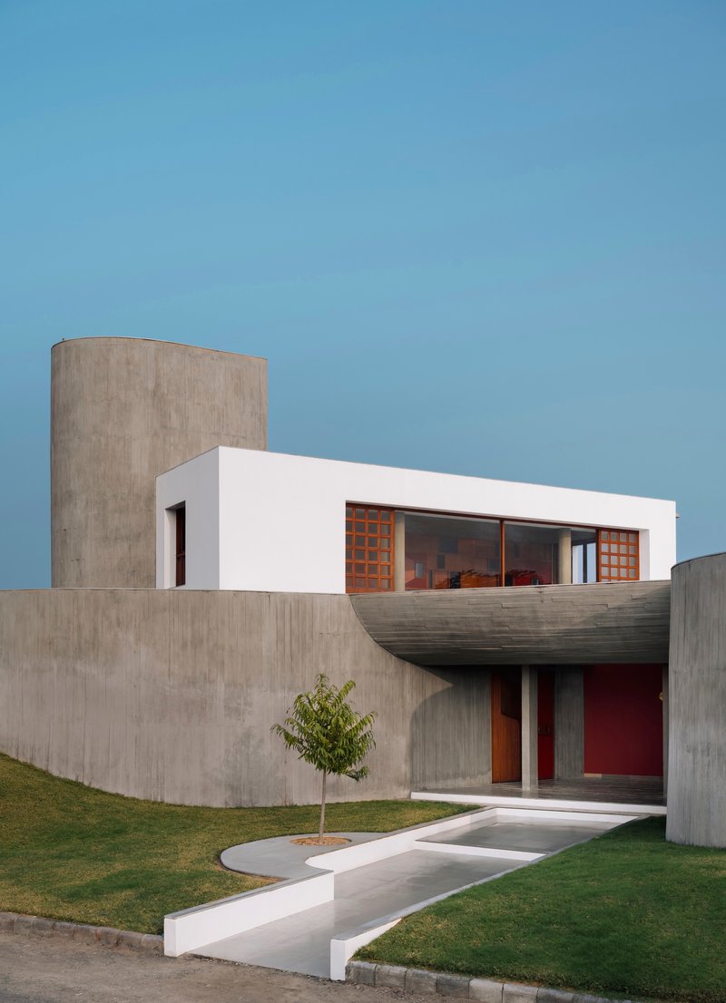 Entrance facade combining board-formed concrete walls with a white rendered upper volume and young tree