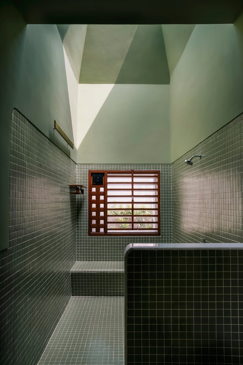 Tiled bathing room with timber louvered window and pyramidal skylight casting shadow patterns