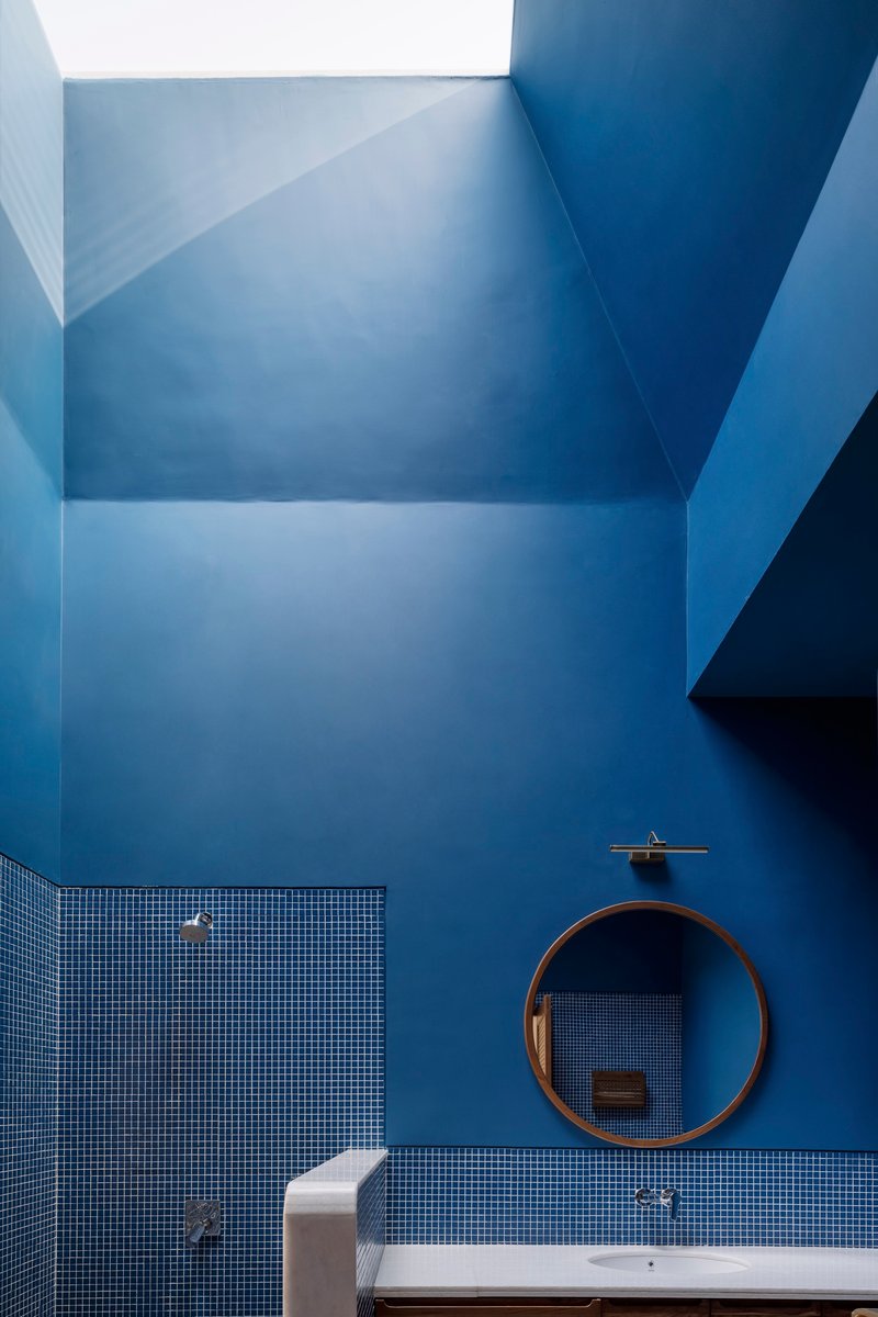 Bathroom skylight well with blue painted surfaces above mosaic tile walls and circular mirror