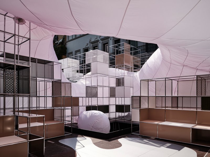 Interior view beneath the tensioned fabric canopy with modular steel shelving and white cube tower element