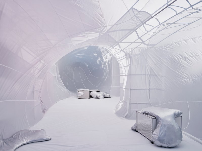 Interior of inflatable bubble with wire frame structure and scattered metallic cushions on white floor