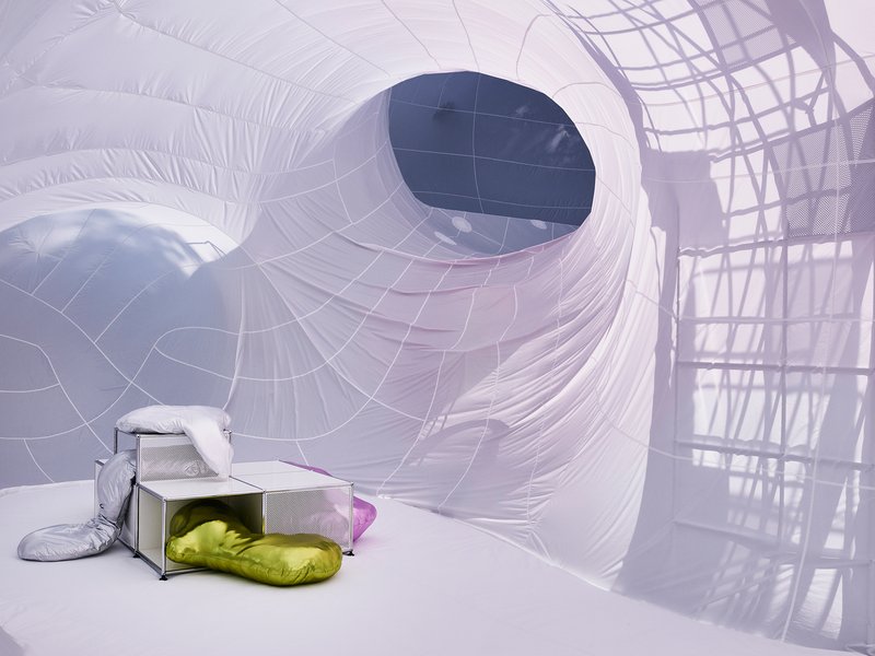 Inflatable chamber with a circular portal and yellow cushions beside metal furniture under soft light