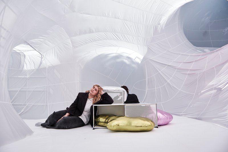 Interior view of white inflatable structures with a person reclining beside metal shelving and gold cushions