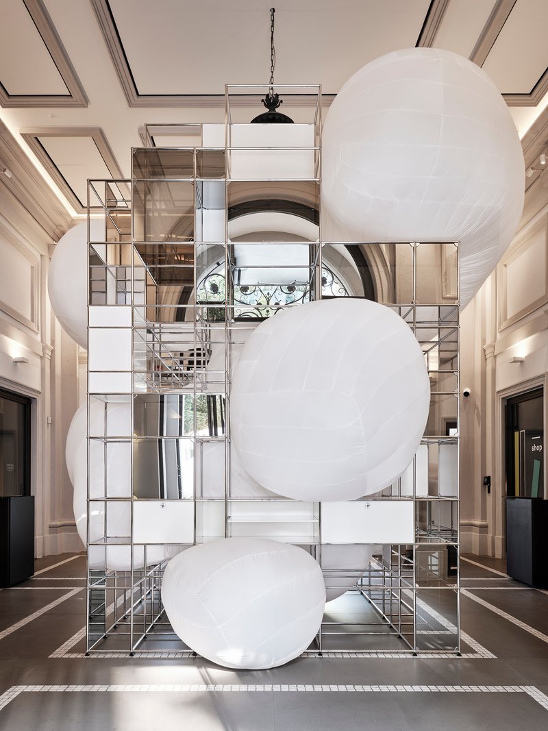 Double-height lobby with suspended white spherical balloons in front of mirrored metal grid storage tower
