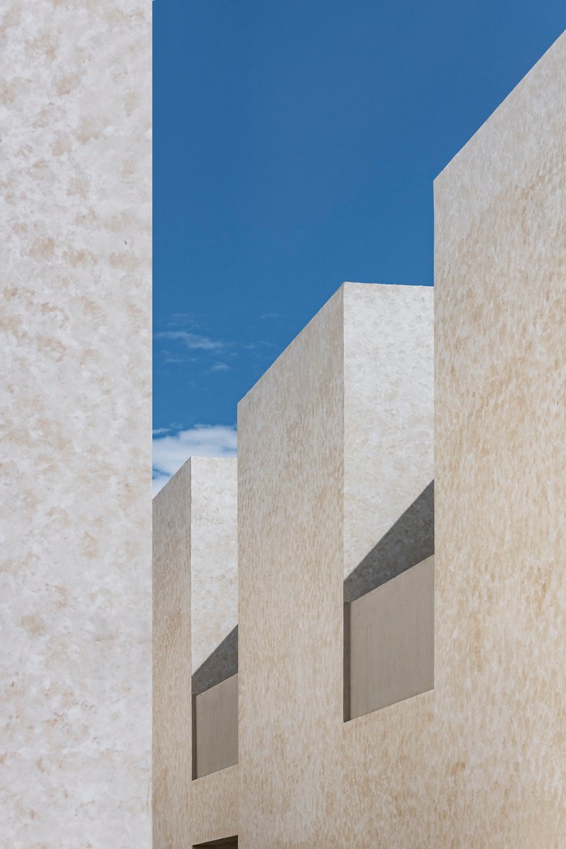 Upward view of pale plastered volumes with deep recessed openings framing blue sky