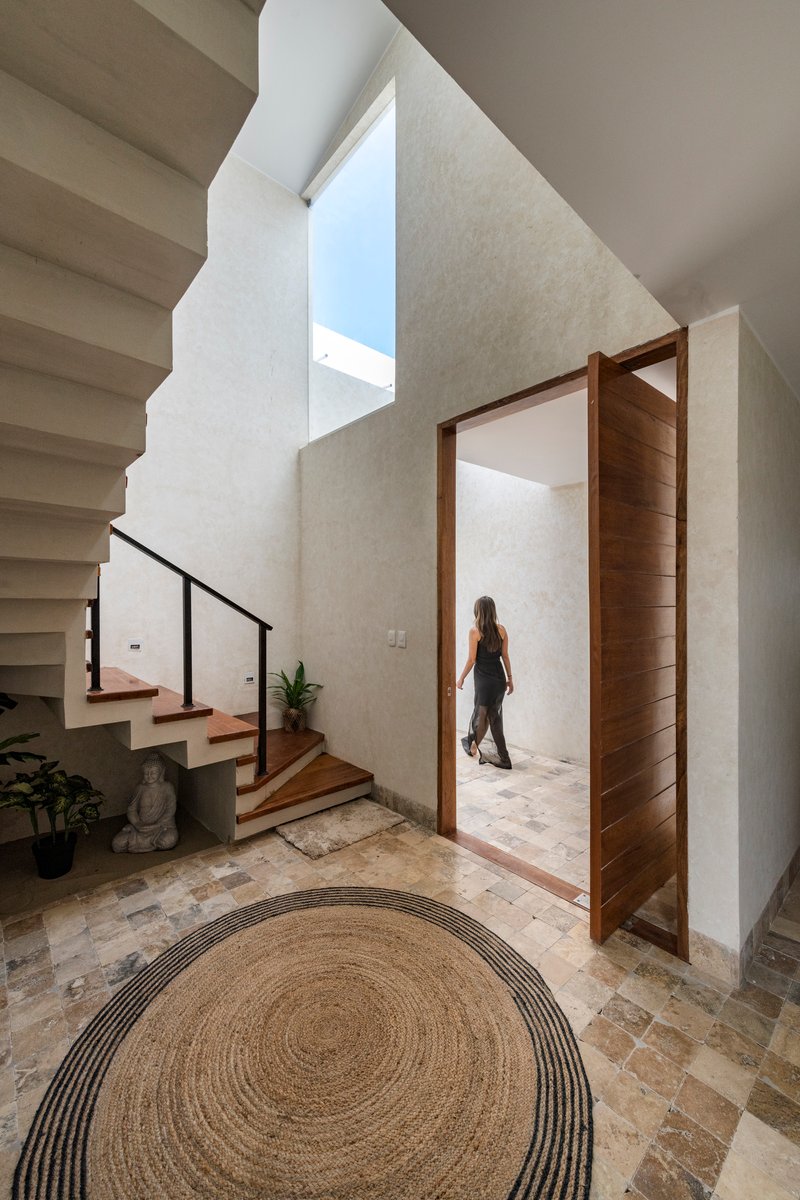 Entry hall with cantilevered staircase, skylight, timber pivot door and a woman passing through