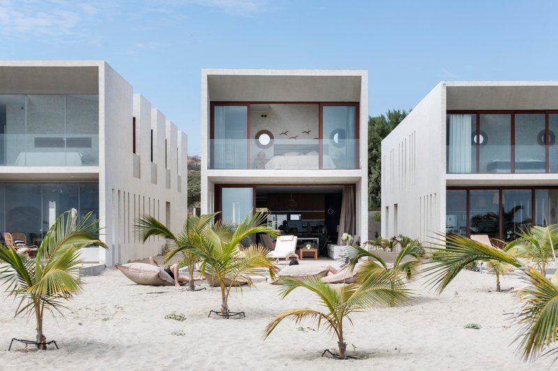 White concrete block facades with vertical slot windows facing a sandy courtyard planted with young palms