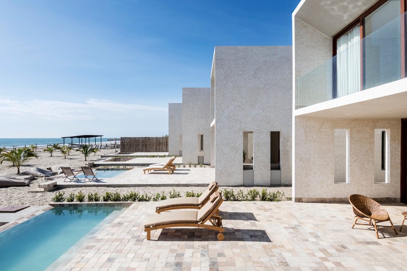 Terrace with stone pavers and rectangular pool beside white textured volumes overlooking the beach
