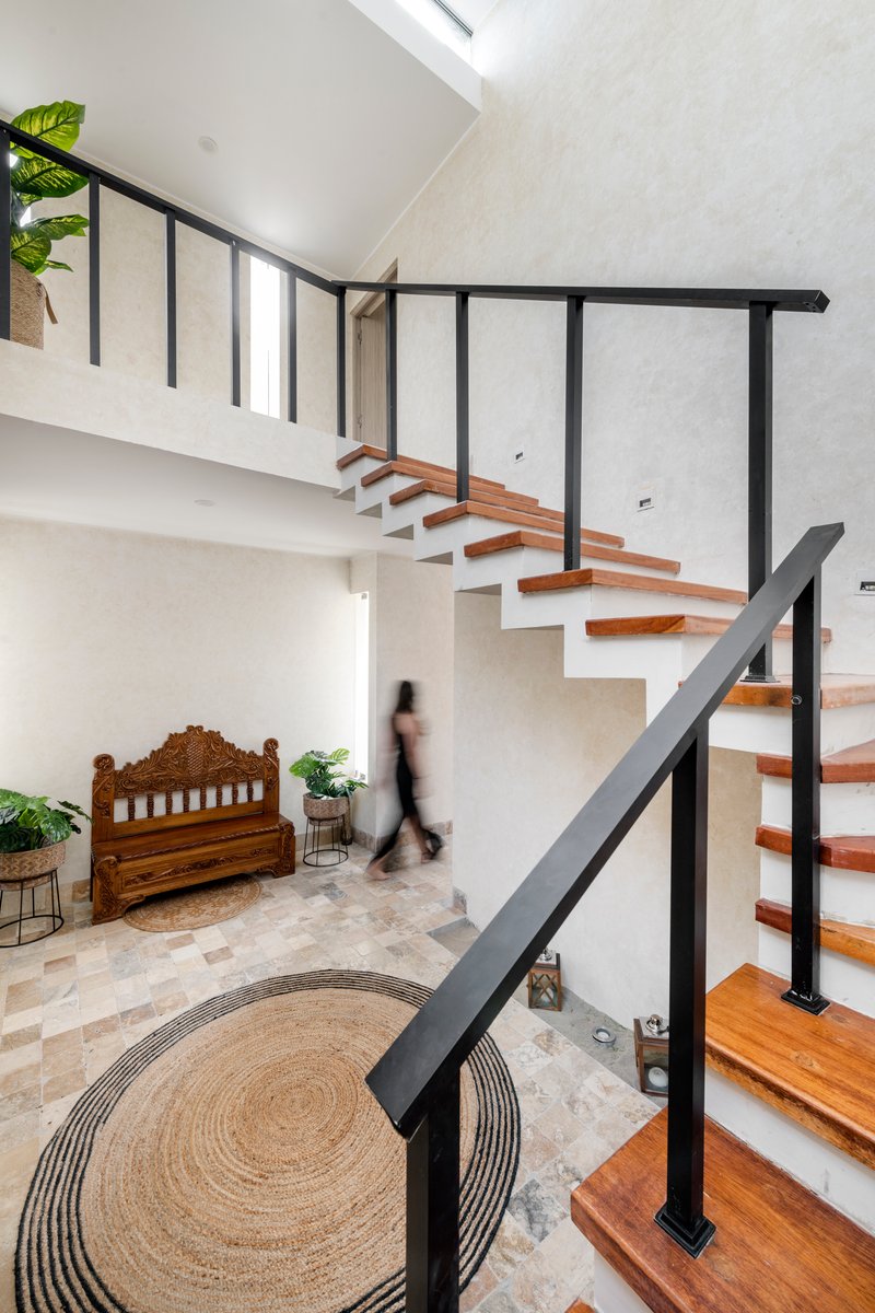 Open-tread staircase with timber treads and black steel railings above a double-height entry hall