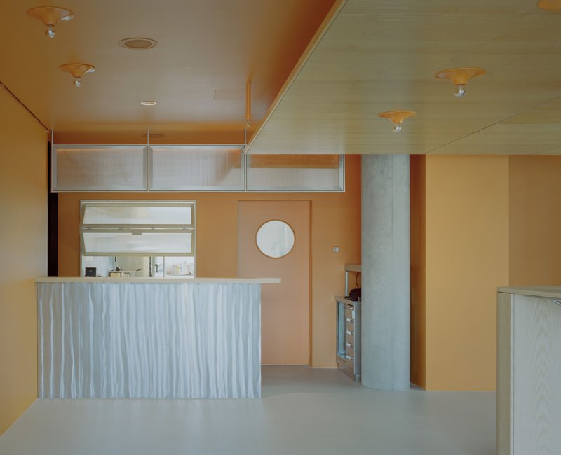 Interior counter with ribbed white panel facing and overhead transom window in peach-toned space