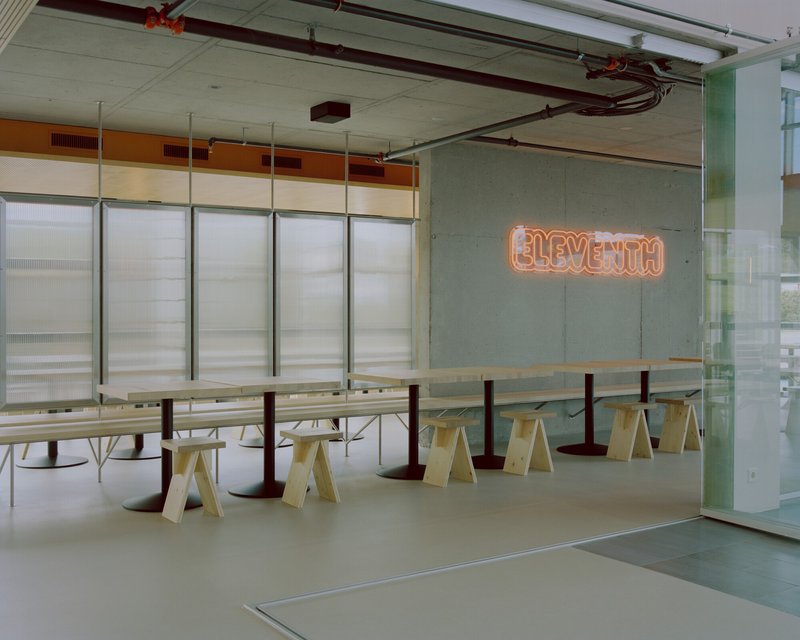 Cafeteria space with orange neon signage mounted on a concrete wall beside translucent partition panels