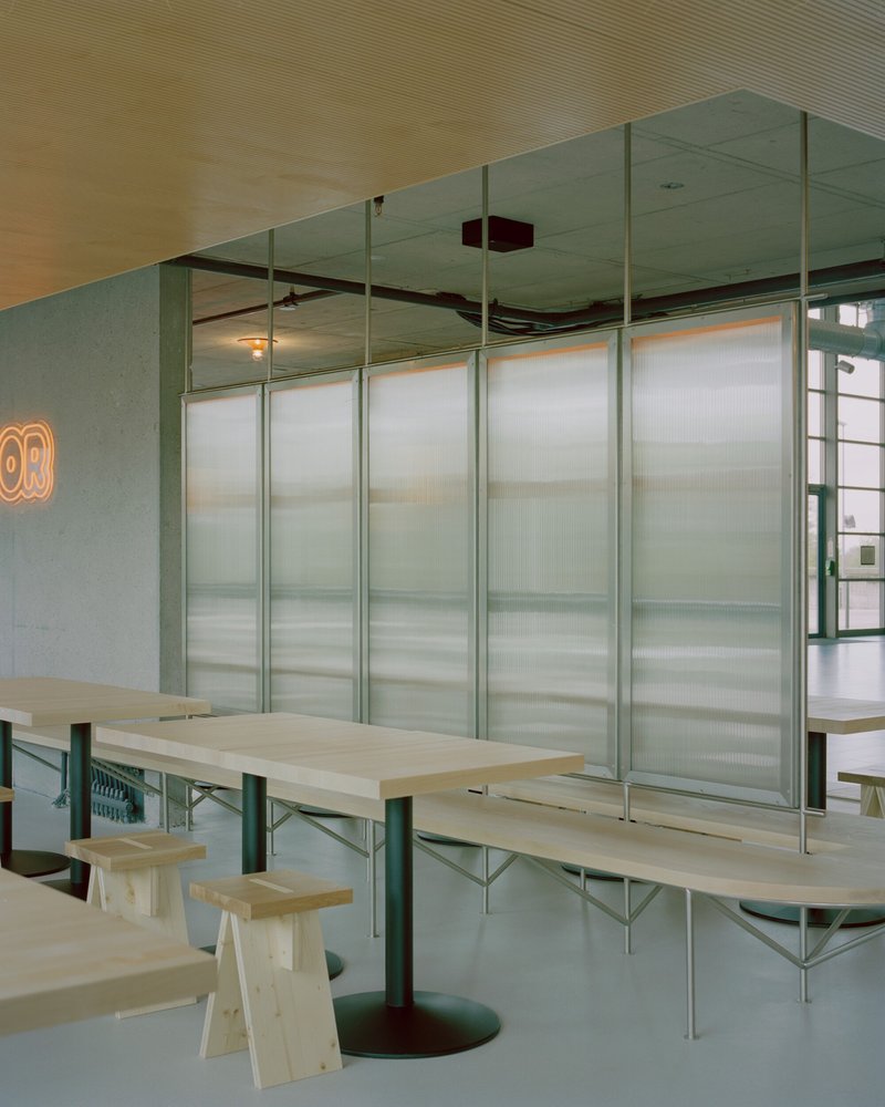 Dining area with plywood tables and translucent corrugated panel partitions on green steel frames
