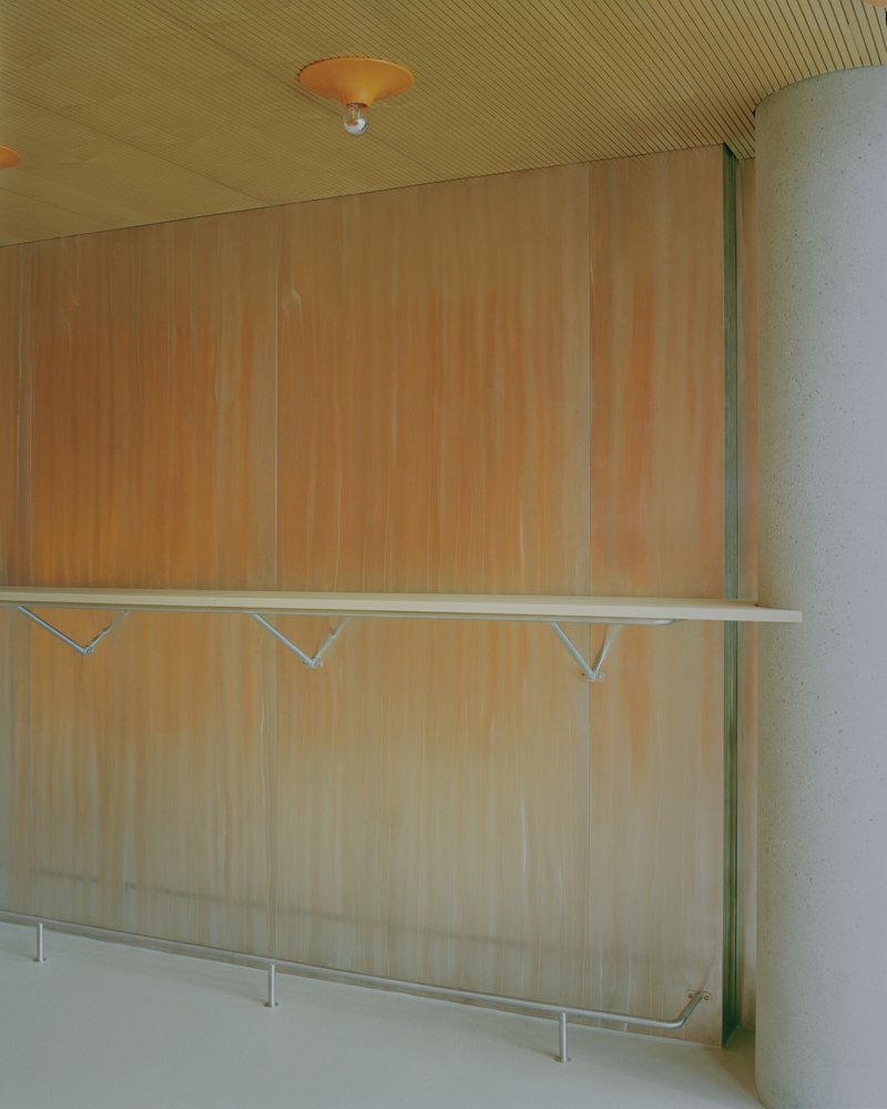 Wall-mounted plywood shelf with tubular steel brackets below slatted ceiling with pendant light