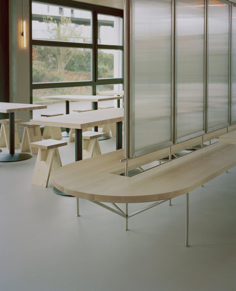 Curved plywood bench beside translucent sliding panels with view to planted greenery beyond window