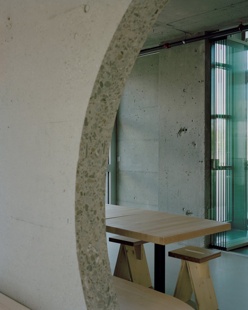 Terrazzo-clad arch framing plywood seating nook with concrete walls and green louvered glazing