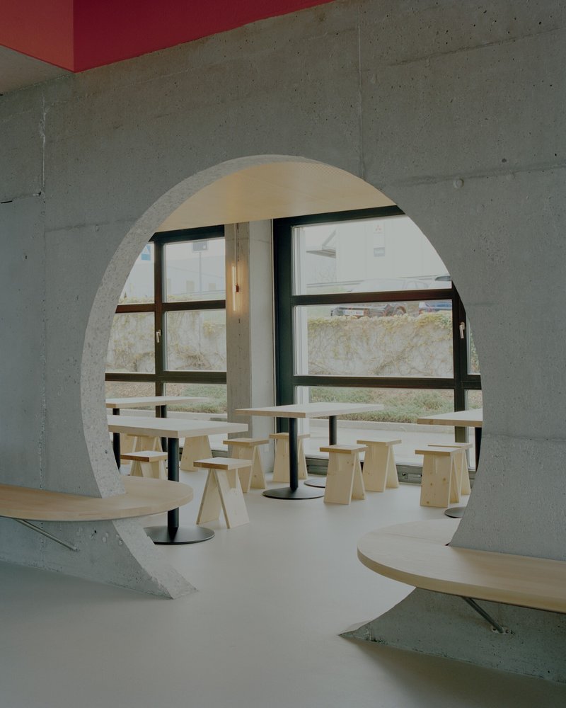 Circular concrete arch framing a dining area with plywood furniture and a red ceiling detail