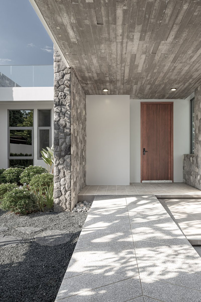 Entry pathway with large concrete pavers and stone wall columns beneath a timber-clad ceiling