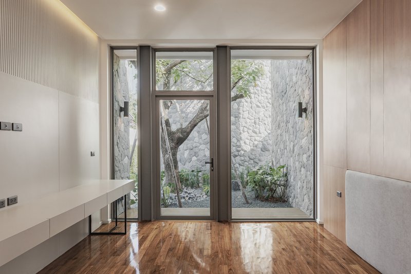 Interior bedroom with timber-lined walls and glass doors opening to courtyard with tree and stone walls