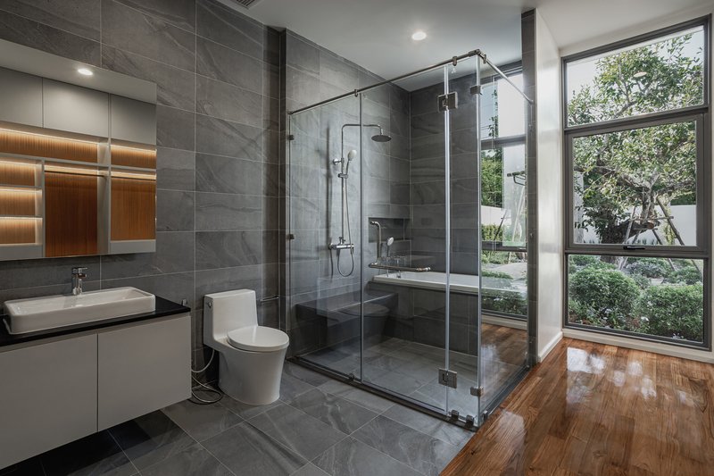 Bathroom with glass-enclosed shower and large window framing views of garden and trees outside