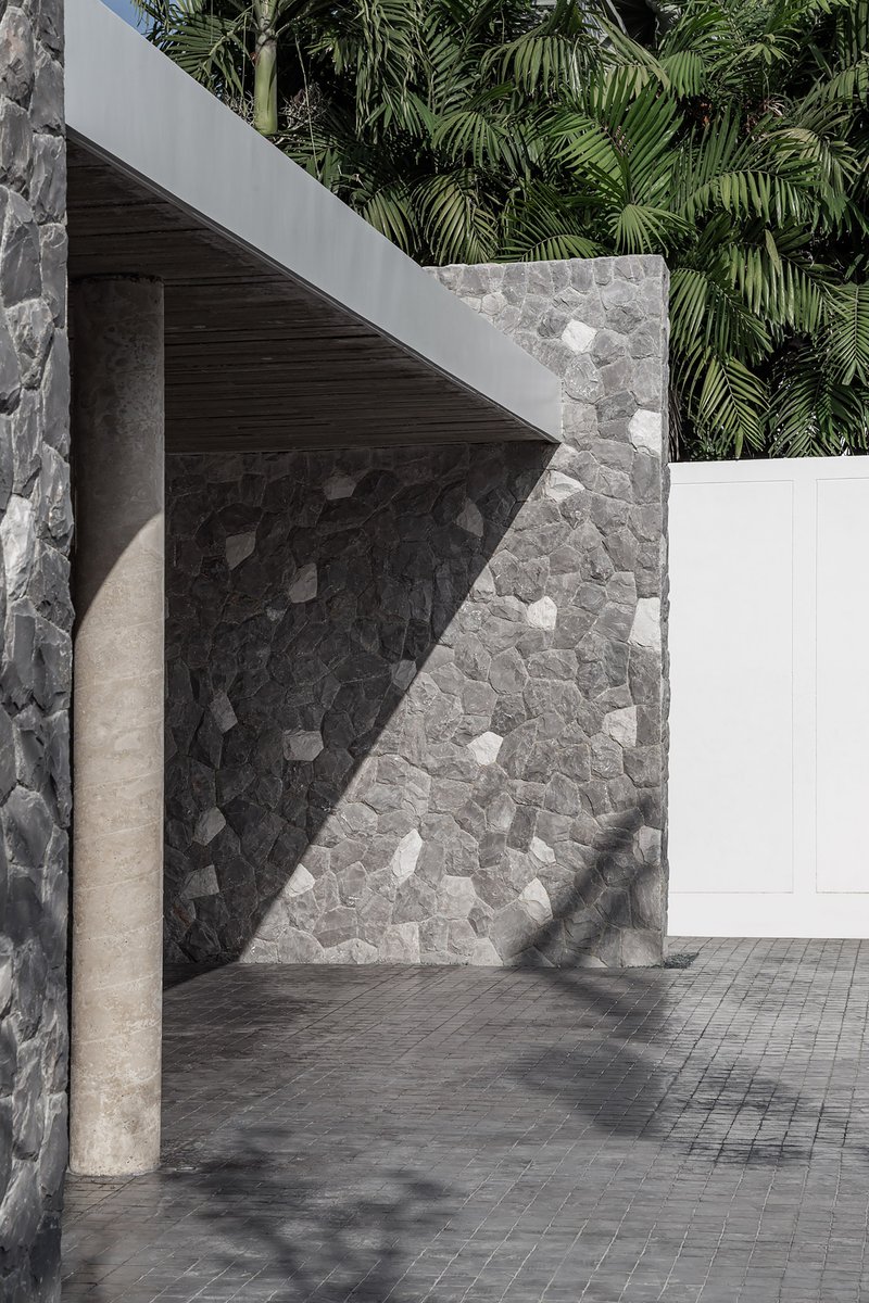 Concrete column beside a stone mosaic wall beneath a timber soffit casting angular shadows