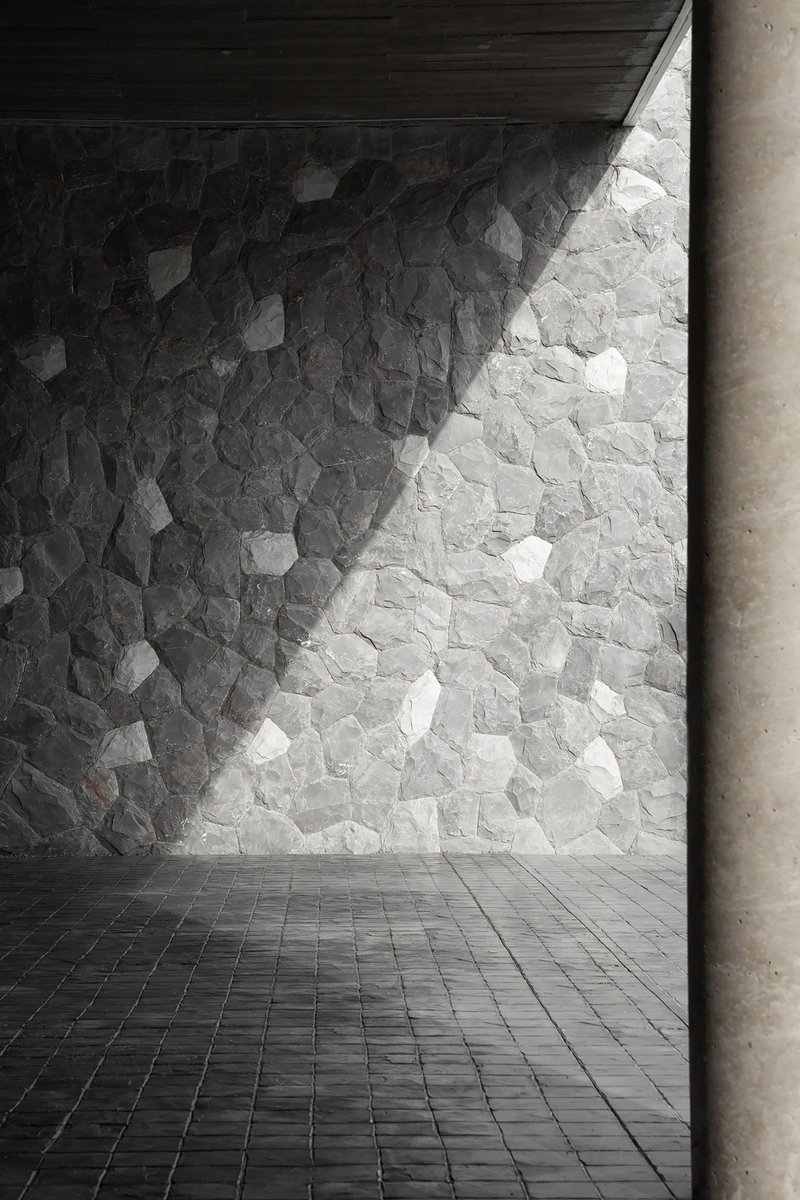 Stone-clad wall with irregular pieces in light and shadow next to a concrete column