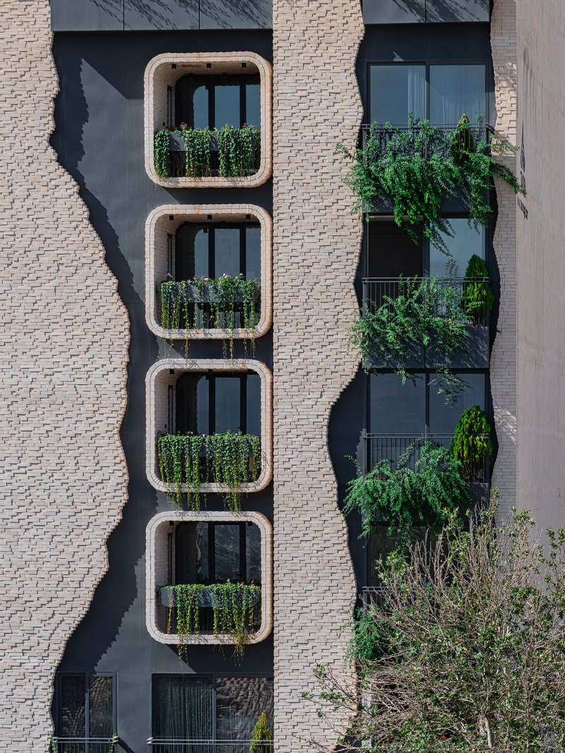 Vertical stack of four rounded-corner balconies with planted railings beside a cascading green facade