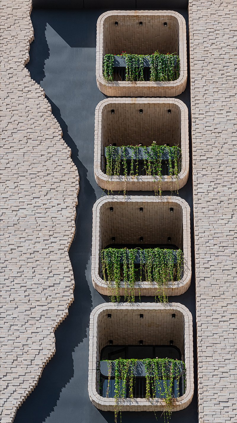 Aerial view of four stacked balconies with exposed brick ceilings and planters between black metal railings