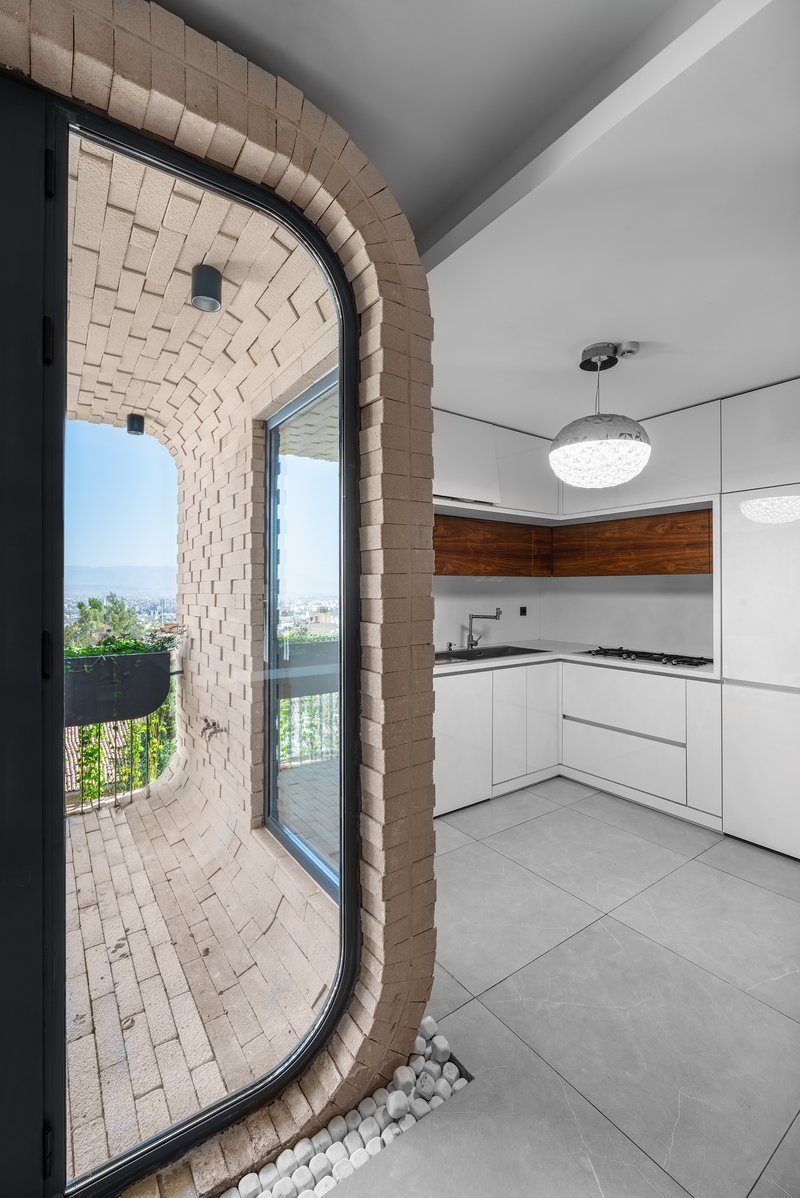 Curved brick archway opening from kitchen onto planted balcony with pebble drainage bed