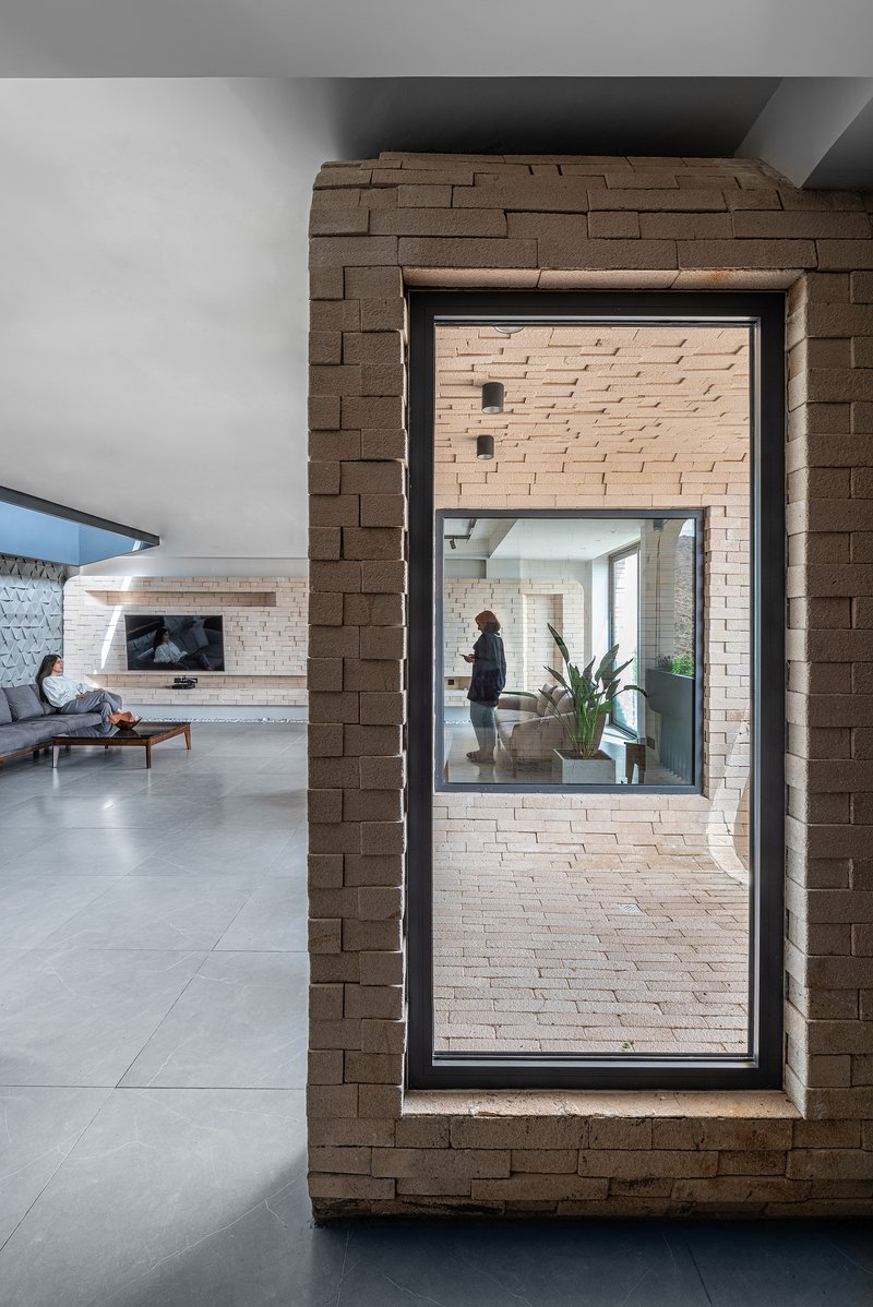 Interior view through brick-framed window opening showing a person standing in adjacent unit