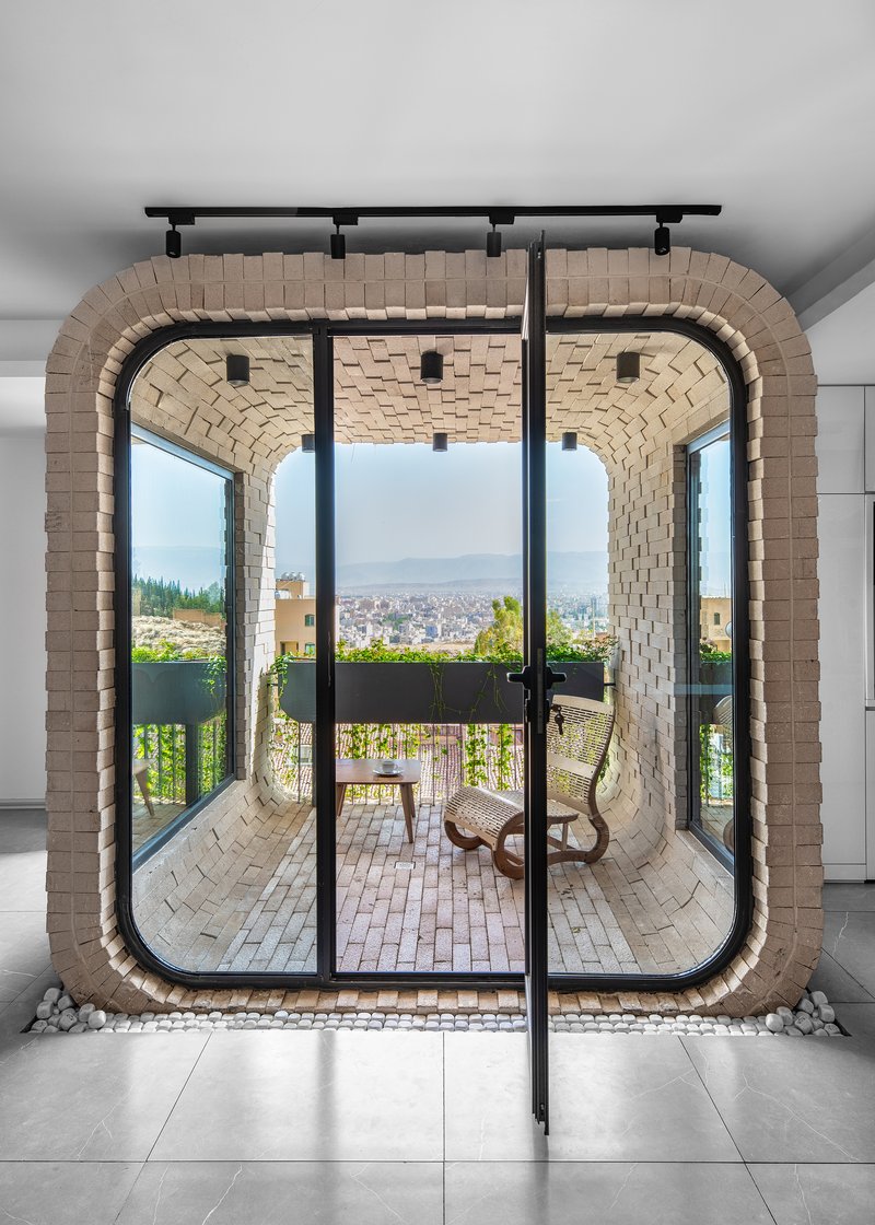 Interior view through glass doors to a vaulted brick balcony with seating and cityscape beyond