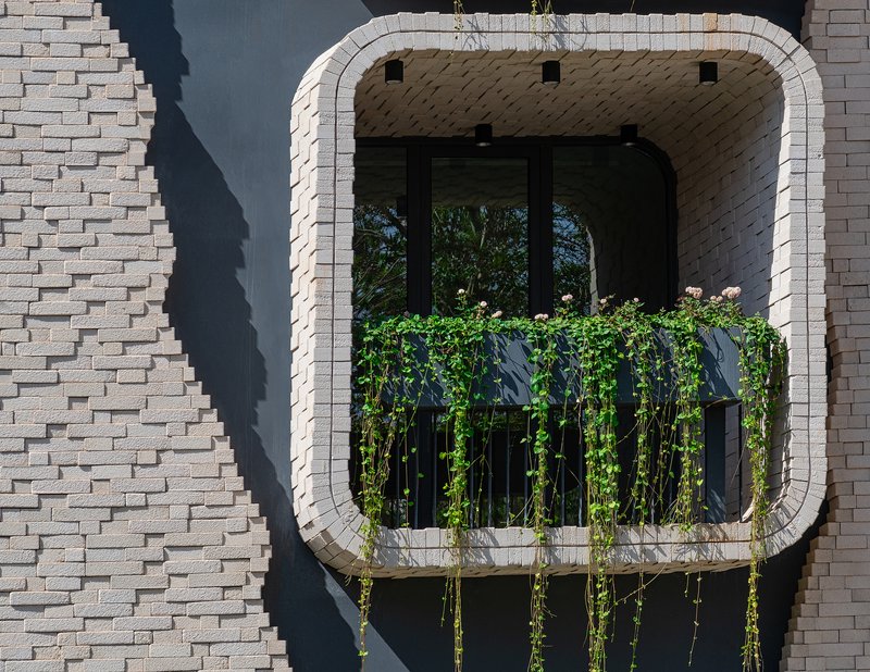Close-up of a single balcony with vining plants on black railings framed by pale brick and recessed glazing