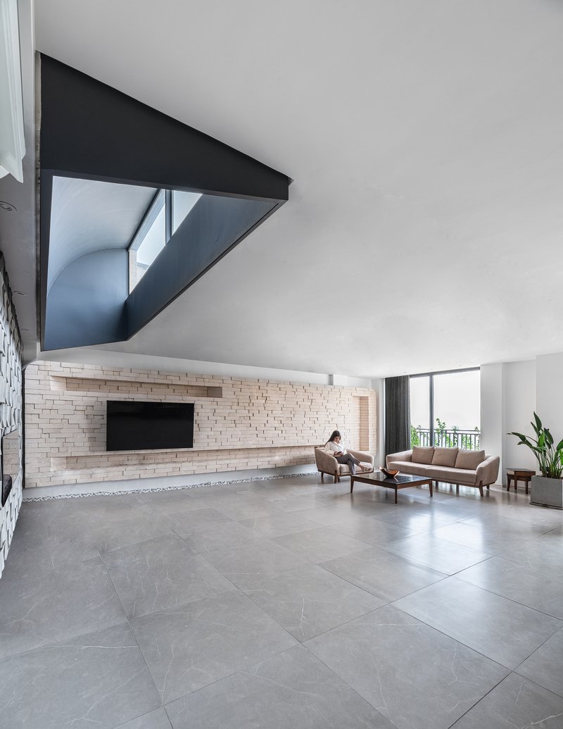 Double-height living room with textured brick wall and triangular black-framed mezzanine opening above