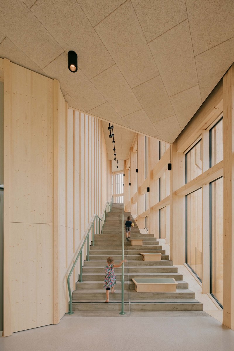 Timber-lined stairwell with diagonal acoustic ceiling panels and child descending the steps