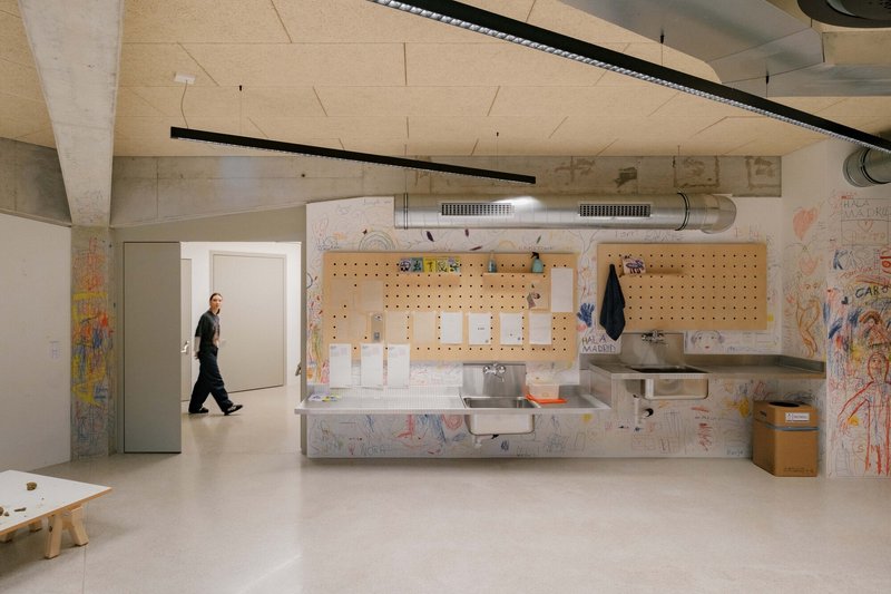 Children's washroom with perforated plywood pegboard and exposed concrete ceiling beams