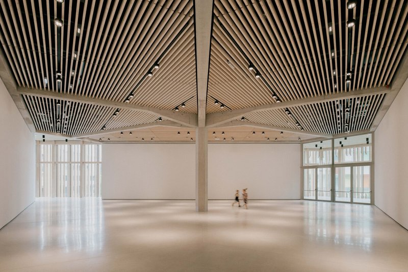Open gallery space with radiating timber slat ceiling and two figures crossing the polished floor
