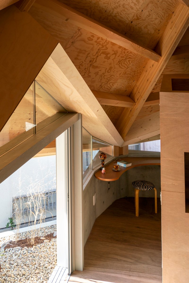 Interior view of plywood-clad volumes beneath exposed timber roof rafters with a person seated at a curved alcove