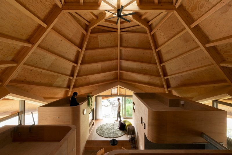 Upward view of the polygonal timber ceiling with exposed beams and central skylight above plywood room modules